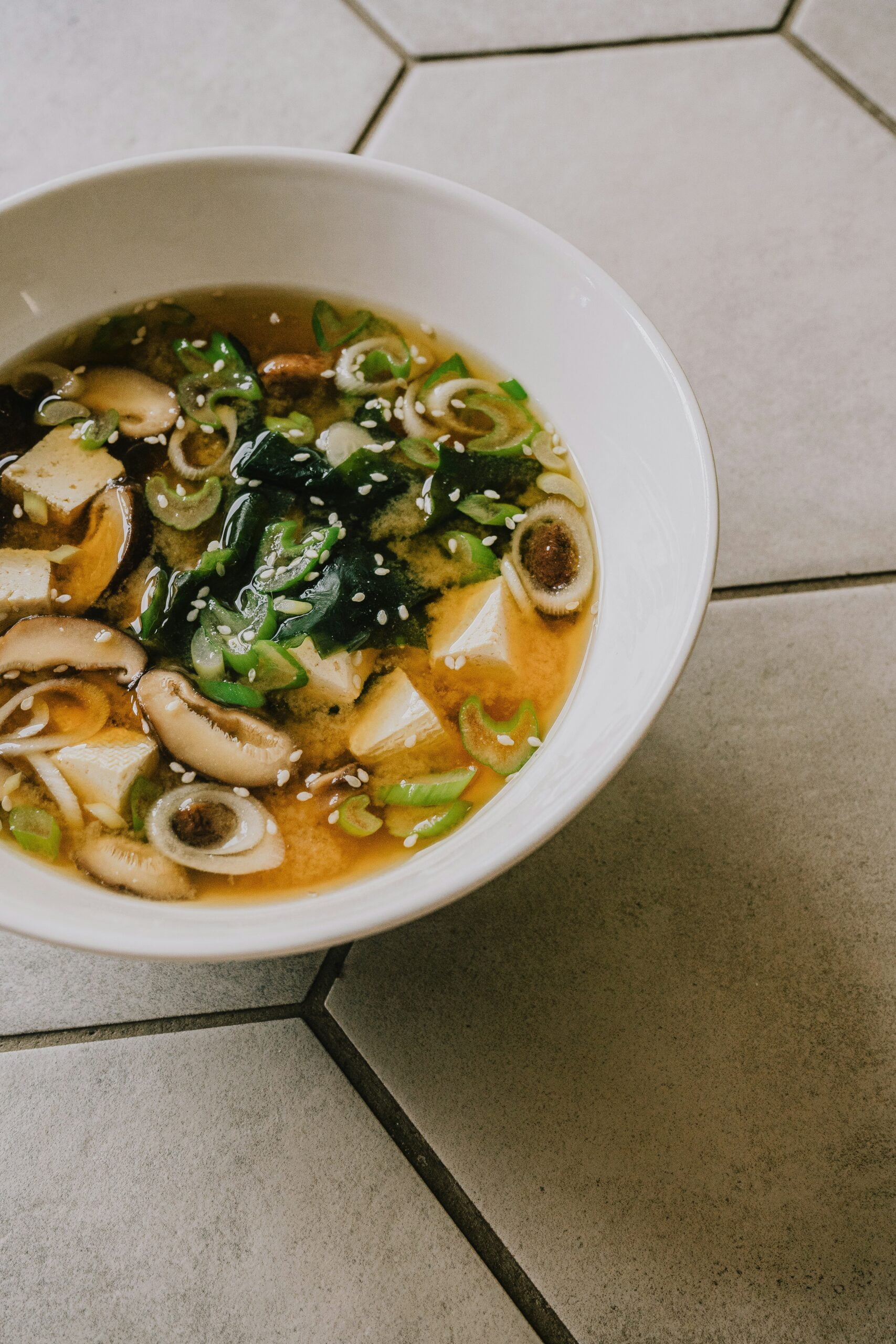 a white bowl filled with soup on top of a tiled floor